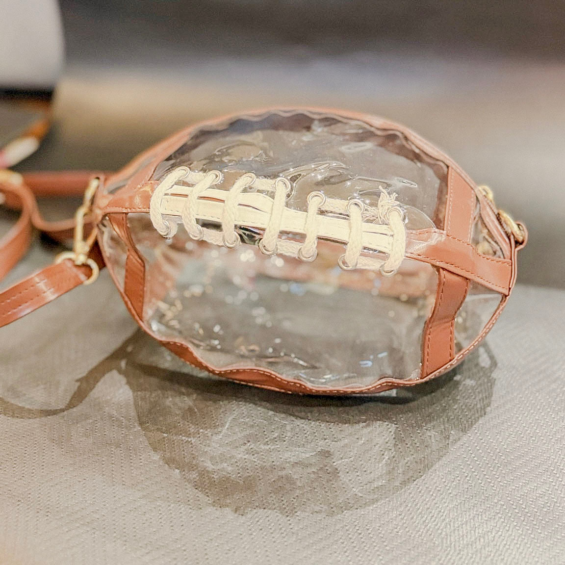 Clear football-shaped game day crossbody purse with brown trim and white laces, front view