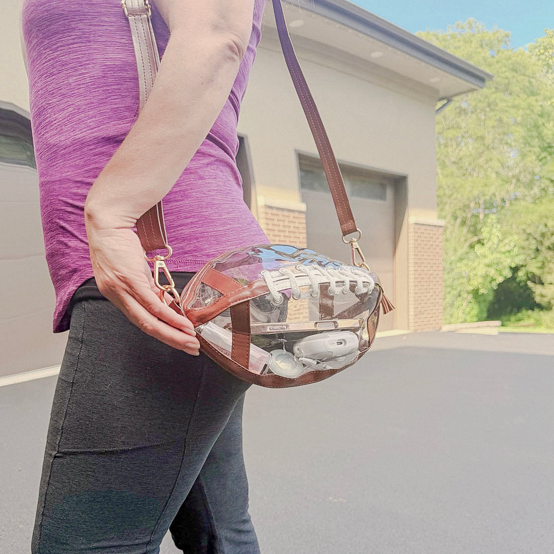 Clear football-shaped crossbody purse worn at the hip with adjustable brown strap